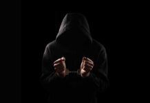 A hooded figure with hands in handcuffs against a dark background