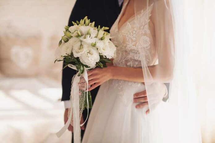 Bride holding a bouquet with groom's hand on her waist