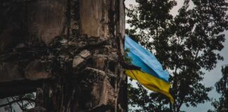 A damaged building with a Ukrainian flag in the background