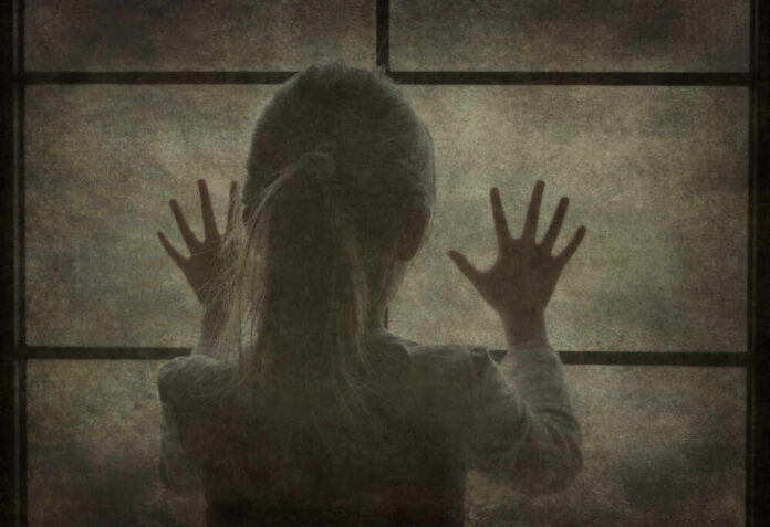 A silhouette of a child with hands pressed against a window