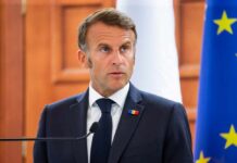 A political leader speaking at a press conference with flags in the background
