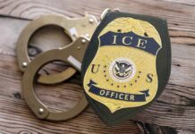 TRUMP’S ICE STRIKE: Terrorist Kin Arrested! ICE officer badge next to handcuffs on a wooden surface