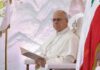 Pope seated in a ceremonial chair with flags in the background