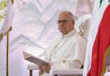 Pope seated in a ceremonial chair with flags in the background