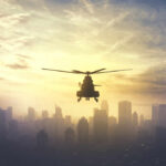 Silhouette of a helicopter flying over a city skyline at sunset