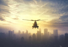 Silhouette of a helicopter flying over a city skyline at sunset