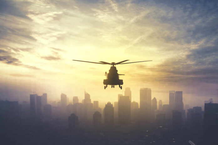 Silhouette of a helicopter flying over a city skyline at sunset