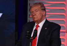 Man in suit at a microphone, red background.