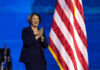Did Klobuchar Botch Justice? Explosive Allegations! Person clapping near American flag on stage.