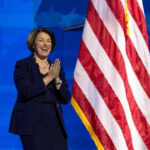 Did Klobuchar Botch Justice? Explosive Allegations! Person clapping near American flag on stage.