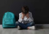 Child sitting upset with backpack and books nearby.