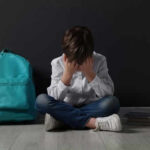 Child sitting upset with backpack and books nearby.