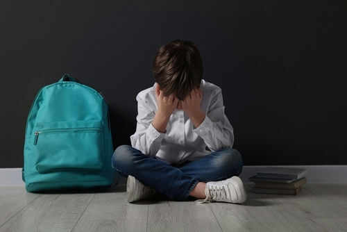 bullying2290581559 Child sitting upset with backpack and books nearby.