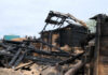 Burned wooden house with collapsed, charred beams and roof remains