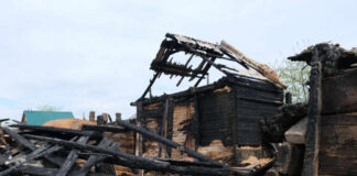 Burned wooden house with collapsed, charred beams and roof remains
