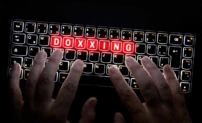 shutterstock_1319411075.jpg Hands typing on a backlit keyboard with the word 'DOXXING' illuminated in red