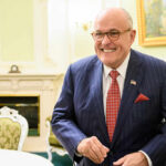 A smiling man in a striped suit standing in an elegantly decorated room