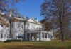 A historic white mansion surrounded by autumn trees and a clear blue sky