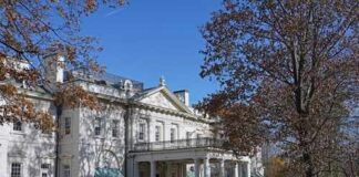 A historic white mansion surrounded by autumn trees and a clear blue sky
