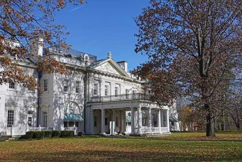 A historic white mansion surrounded by autumn trees and a clear blue sky
