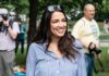 A smiling woman in a striped shirt at an outdoor event with photographers in the background