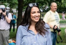 AOC’s Bold Moves: White House or Senate? A smiling woman in a striped shirt at an outdoor event with photographers in the background