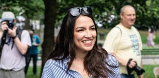 A smiling woman in a striped shirt at an outdoor event with photographers in the background