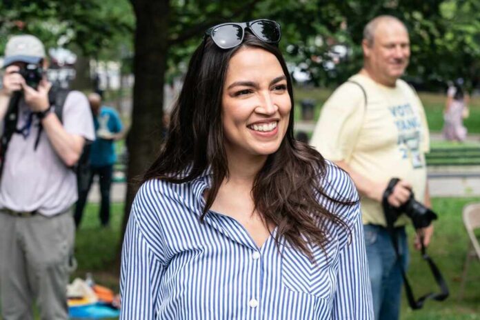 A smiling woman in a striped shirt at an outdoor event with photographers in the background