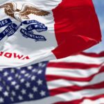 Iowa state flag in front of the American flag, both waving in the wind