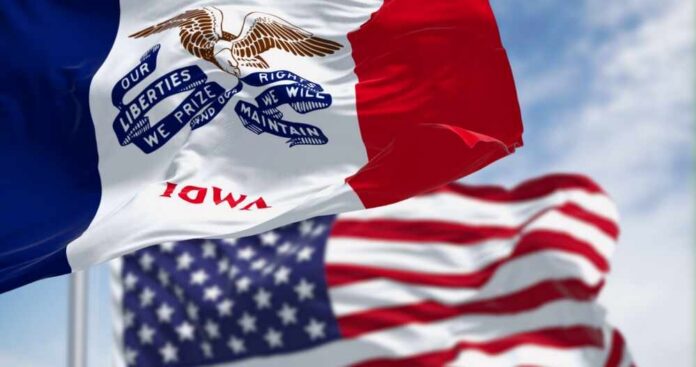 Iowa state flag in front of the American flag, both waving in the wind