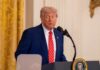 Ballroom Controversy Clouds Healthcare Event A man in a suit speaking at a podium in a formal setting