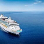 A large cruise ship sailing on a calm ocean under a clear blue sky