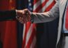 Trump’s Beijing Visit: Are US Interests at Risk? Two individuals shaking hands in front of flags