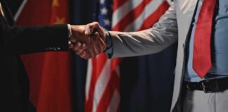 Two individuals shaking hands in front of flags