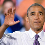 A speaker gesturing with one hand while addressing an audience