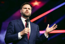 Vice President Blasts Religious Hatred and Politics Man in suit speaking with microphone on stage.