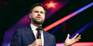 Man in suit speaking with microphone on stage.