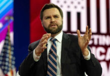 Man in suit speaking on stage with gesturing hands
