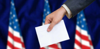 Hand placing envelope into ballot box with flag background