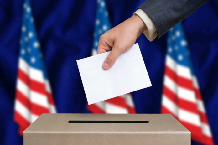 Hand placing envelope into ballot box with flag background
