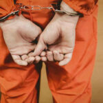 Paid Rape Plot—Fire Chief Unmasked Person in orange jumpsuit with handcuffs behind back