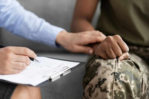 Person comforting someone in military uniform with clipboard