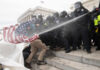 Police in riot gear spray crowd with water on government building steps