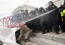 Police in riot gear spray crowd with water on government building steps