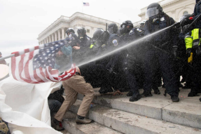 Police in riot gear spray crowd with water on government building steps