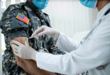 Outbreak Sparks Blame Game — Facts Still Missing A healthcare professional administering a vaccine to a soldier