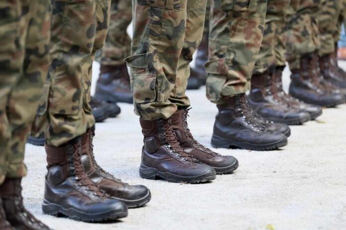Military,Boots,On,The,Legs,Of,Soldiers,In,A,Row. Row of soldiers in camouflage uniforms standing at attention with military boots