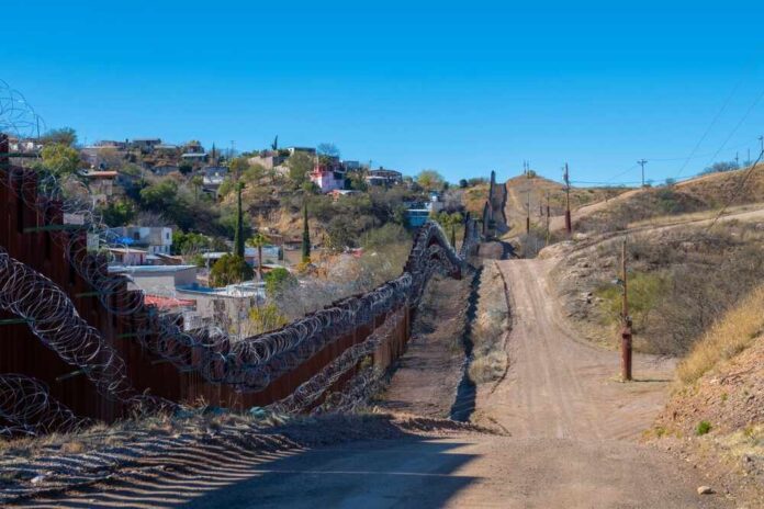 United,States,Mexico,Border,Wall,Between,Nogales,Arizona,And,Nogales A border wall with barbed wire in a rural landscape