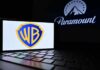 Warner Bros logo displayed on a smartphone with Paramount logo in the background