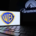 Big Media Just Got Bigger — Guess Who Wins Warner Bros logo displayed on a smartphone with Paramount logo in the background